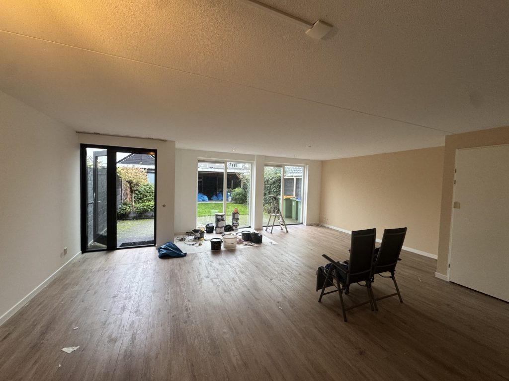 Ruime woonkamer met tuindeuren, verfemmers en een trapje klaar voor het behangwerk