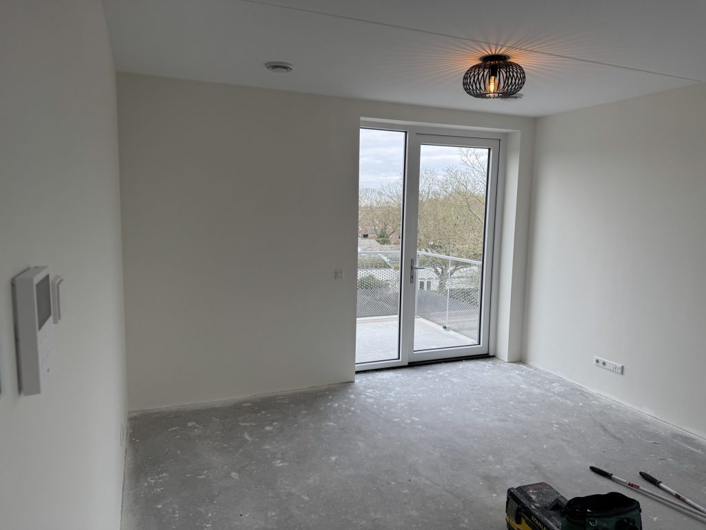 Lege kamer in een nieuw appartement met balkondeur, kort na de oplevering